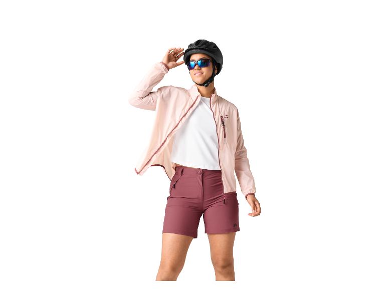 Vrouw in roze jasje, wit T-shirt en bordeauxrode shorts, met zwarte helm en zonnebril.
