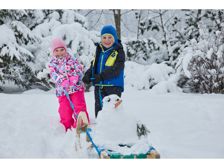 Twee kinderen in winterkleding met een slee en een kleine sneeuwpop in een besneeuwd landschap.