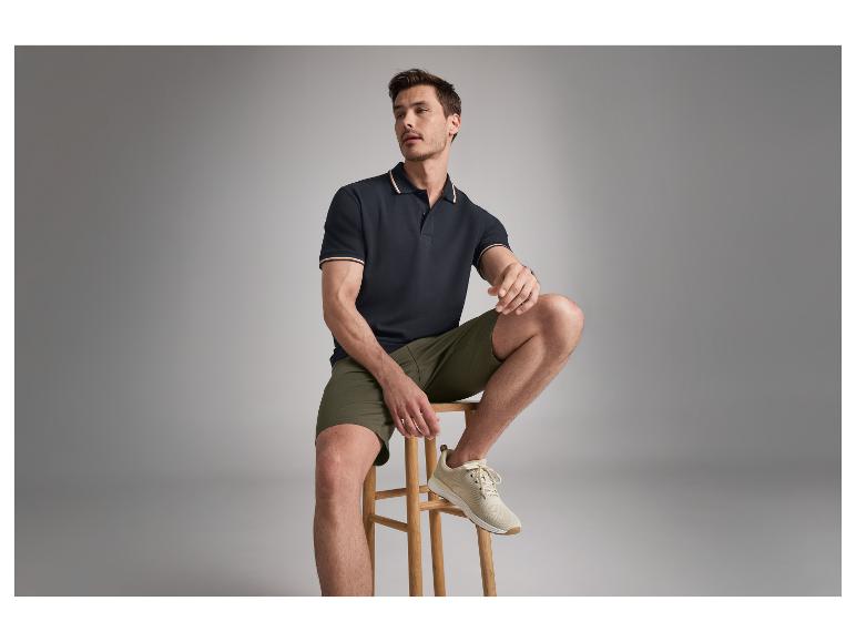 Een mannelijk model draagt een donkerblauwe polo en olijfgroene shorts.