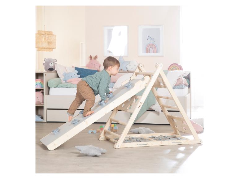 Peuter klimt op een houten klimrek in een kinderkamer met bed en decoratie.
