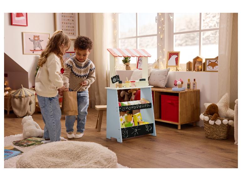 Twee kinderen spelen met een houten marktkraam en speelgoed in een feestelijk versierde kamer.