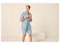 Lachende man in lichtblauw zomerpyjama, overhemd met korte mouwen en korte broek.