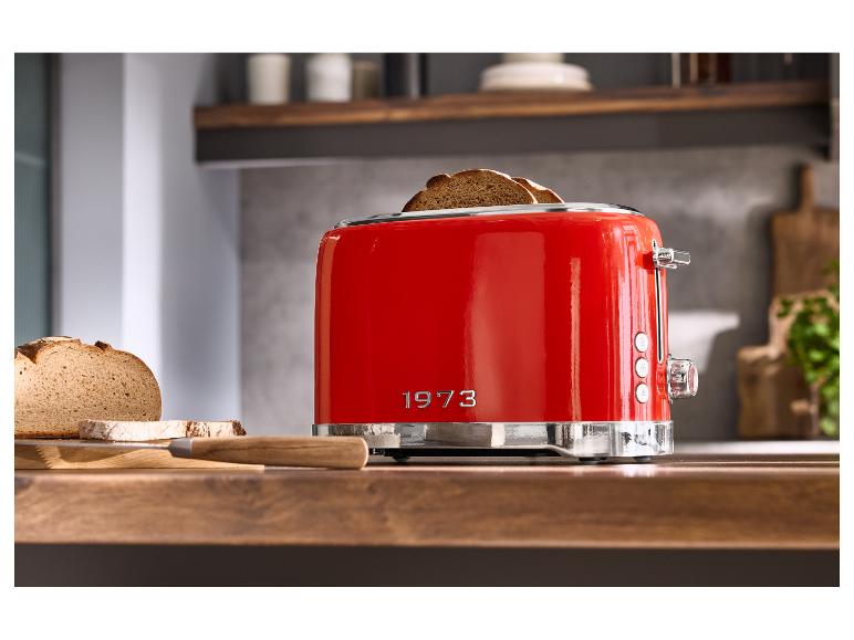 Rode retro broodrooster met sneetjes brood op een houten aanrecht, met '1973' in reliëf.