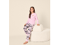 Meisje in roze shirt met lange mouwen en croissantafbeelding en roze geruite pyjamabroek, zittend op een crèmekleurige kruk.