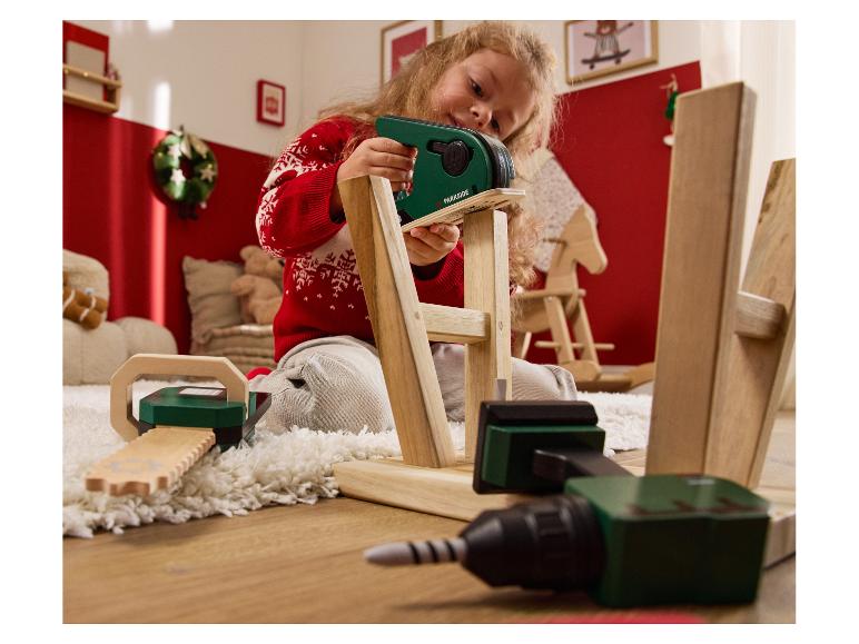 Een meisje speelt met een Parkside speelgoedgereedschapset, inclusief een zaag en een boormachine.
