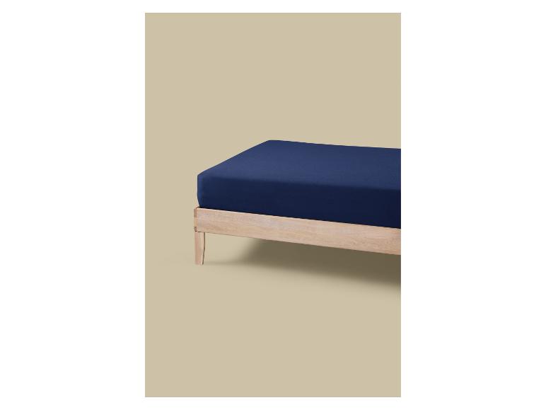 Een donkerblauw matras op een licht houten frame tegen een beige achtergrond.