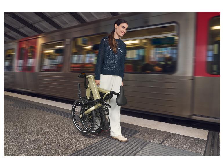 Vrouw met een opvouwbare fiets op een treinstation terwijl een trein voorbijrijdt.