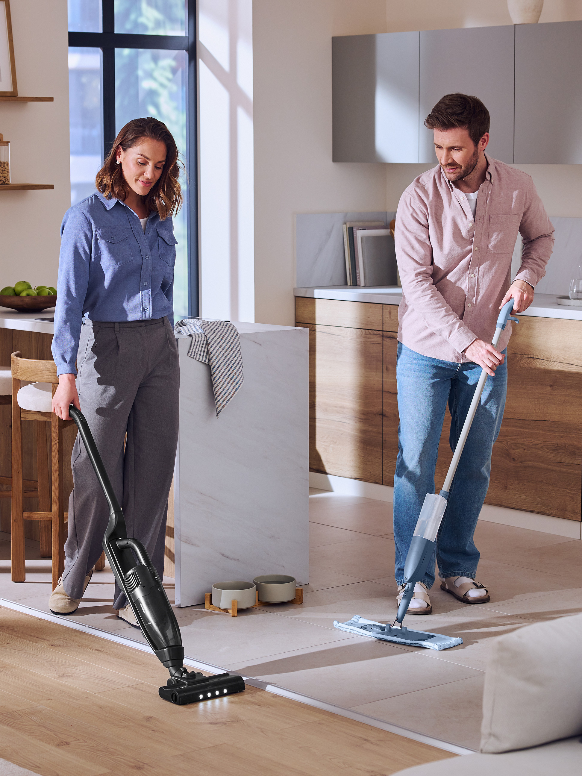 Een stel maakt de keukenvloer schoon met een steelstofzuiger en dweil.