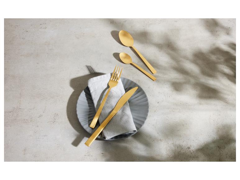 Gouden bestek op een grijs bord met linnen servet op een betonnen achtergrond.