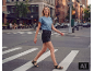 Een vrouw in een blauw T-shirt en zwarte denim short loopt over een zebrapad in de stad.
