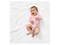 Baby in roze romper op een wit kleed.