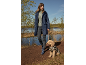 Vrouw in marineblauwe regenjas en rubberen laarzen wandelt met hond in luipaardprint jas bij meer.