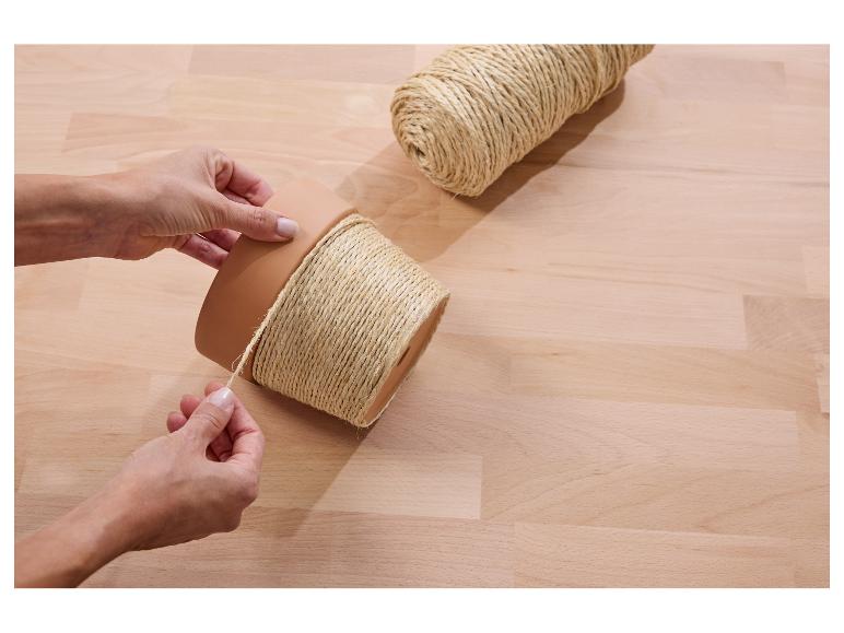 Handen wikkelen touw om een bloempot op een houten tafel, met een rol touw ernaast.