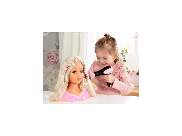 Een jong meisje stylet het haar van een Bayer Design Charlene opmaakpop met een speelgoedföhn.