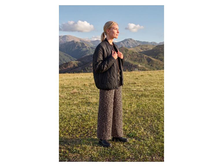 Vrouw in een zwarte gewatteerde jas en broek met luipaardprint in een berglandschap.