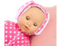 Een roze babypop met witte stippen, liggend op een roze kussen.
