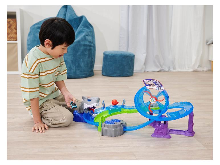 Een kind speelt met een Hot Wheels Shark Cyclone racebaan op een houten vloer.