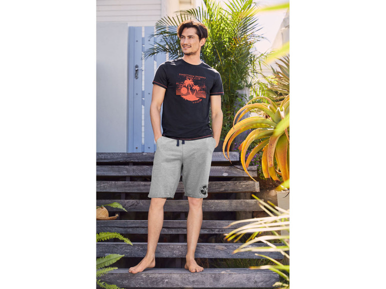 Man draagt een zwarte t-shirt met een print en grijze korte broek.