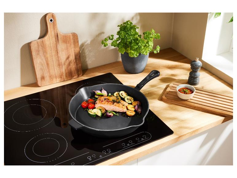 Een zwarte koekenpan met zalm en groenten op een inductiekookplaat.