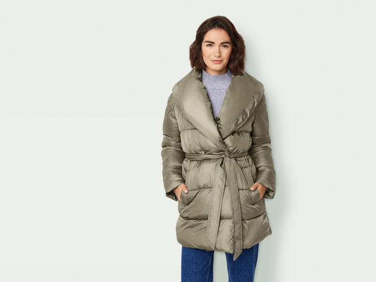 Een vrouw draagt een groene gewatteerde jas met een riem.