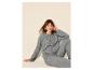 Vrouw in grijze gebreide trui en broek, zittend tegen een beige achtergrond.