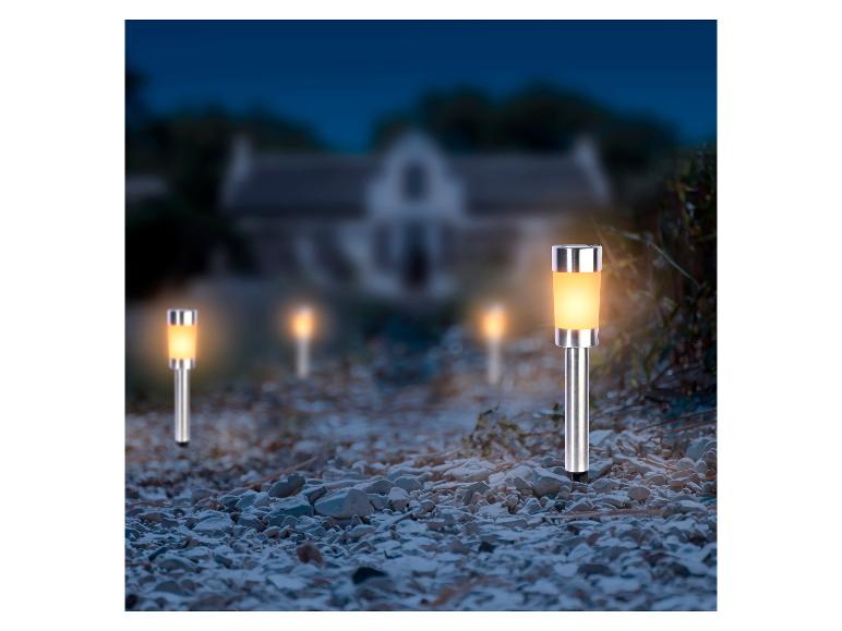 Solar tuinlampen verlichten een kiezelpad naar een huis in het donker.