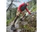 Een vrouw in een rood vest en bloemenleggings loopt over een bergpad.