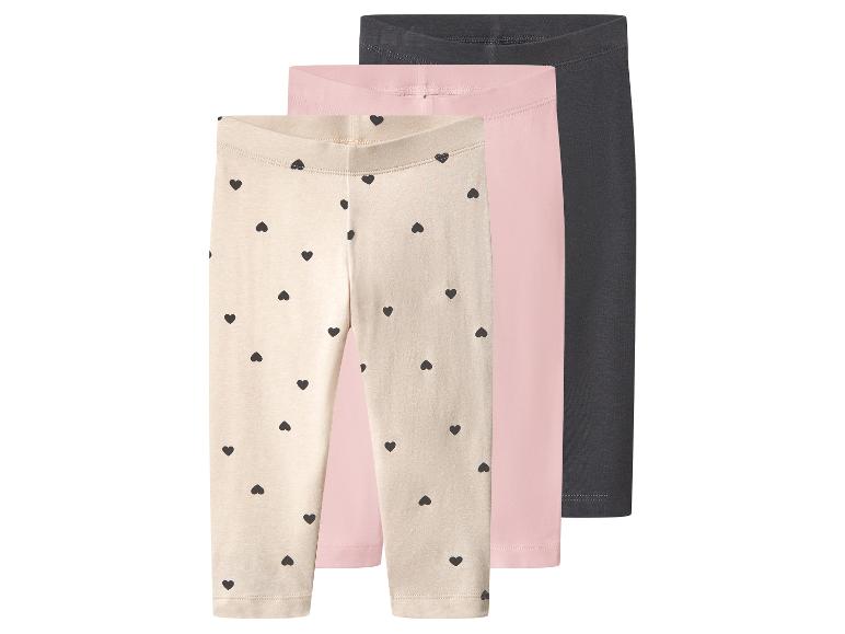 Drie kinderleggings: één beige met zwarte hartjes, één roze en één donkergrijs.