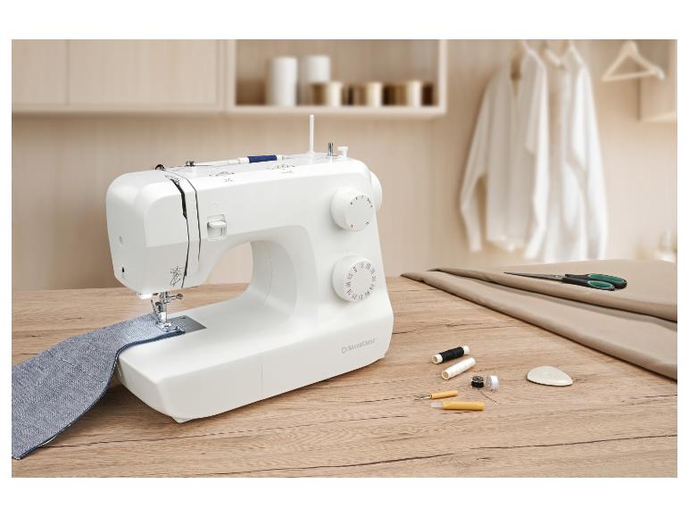 Naaimachine met blauwe stof, schaar en draden op een houten tafel.