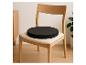 Lichte houten stoel met zwart rond zitkussen in een minimalistisch interieur.