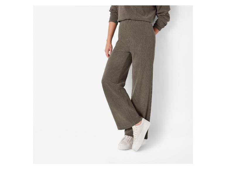 Een model draagt ​​groene corduroy broek en witte sneakers.