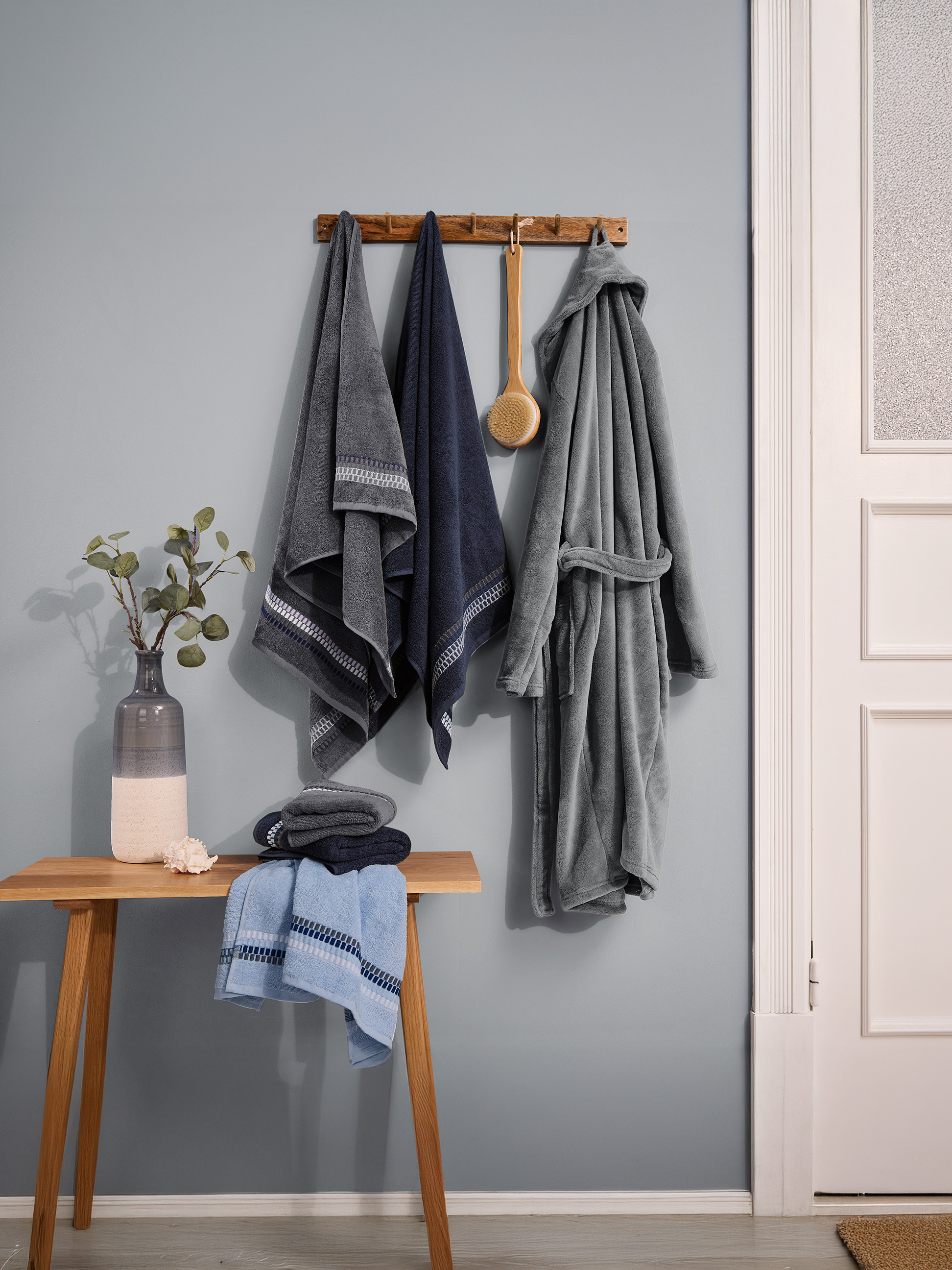 Handdoeken en badjas in blauwe en grijze tinten, hangend aan de muur.