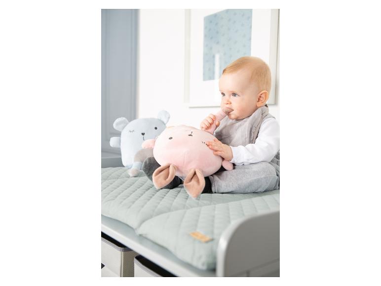 Een baby zit op een commode met twee knuffels, een roze en een blauwe.