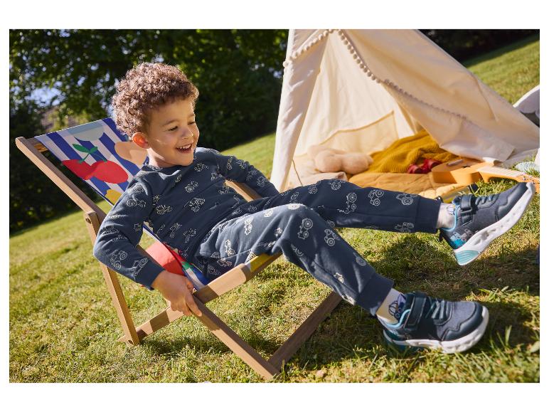 Een jongetje geniet van een zonnige dag zittend in een houten strandstoel met kersenprint.