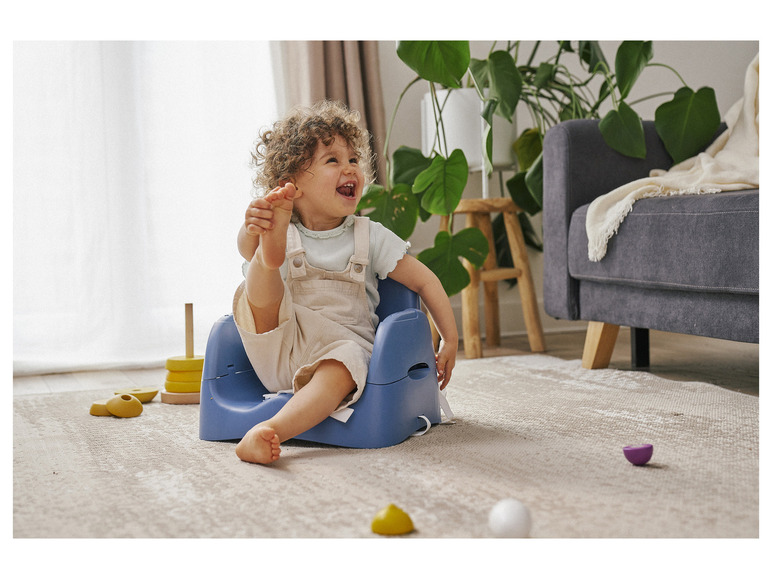 Een baby zit in een blauwe kinderstoel en lacht.