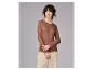 Vrouw in een bruine top met lange mouwen en lichtbeige broek, opzij kijkend.