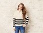 Een jonge vrouw draagt een gestreepte trui en jeans tegen een witte bakstenen muur.