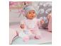 Babypop in roze onesie met muts, fles en speen op een bed.
