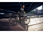 Man in sportkleding op een elektrische fiets onder een brug.