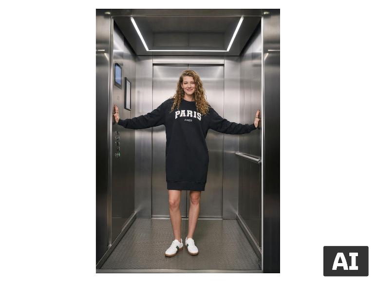 Vrouw in ESMARA® Dames Sweatkleed met de tekst 'PARIS AIMÉE' in een lift. [AI-gegenereerde afbeelding]