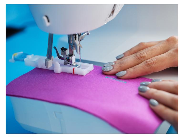 Vrouw naait paarse stof met naaimachine.