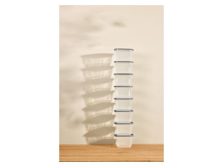 Een hoge stapel doorzichtige plastic voedselbewaarbakjes met grijze deksels op een houten ondergrond.