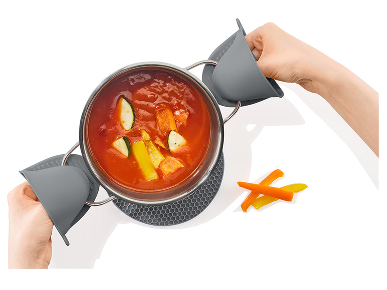 Een pot soep met grijze siliconen potvangers en een hittebestendige onderzetter.