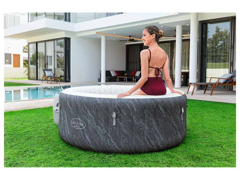 Een vrouw in badkleding ontspant in een opblaasbaar Lay-Z-Spa jacuzzi in de tuin.