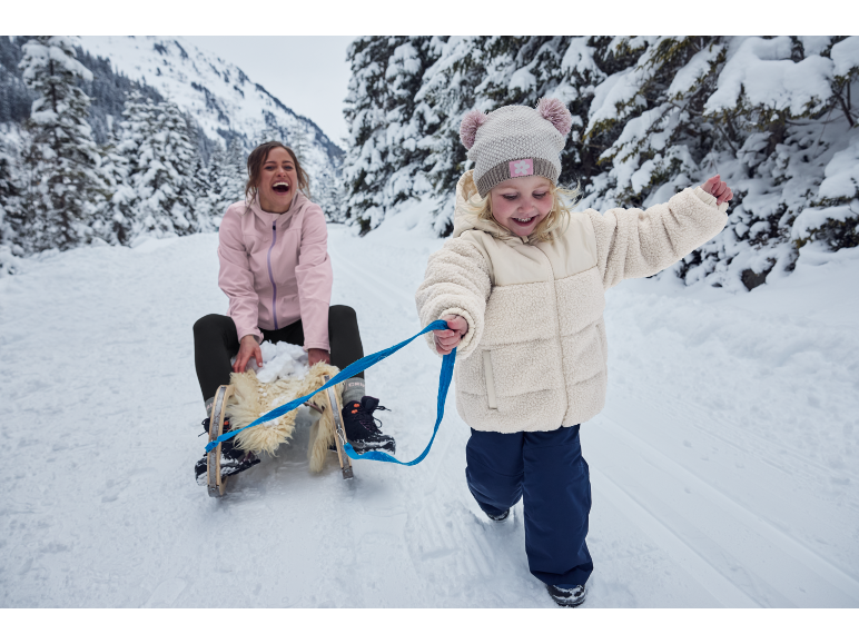Moeder en kind in een besneeuwd landschap, het kind trekt een slee met de moeder.