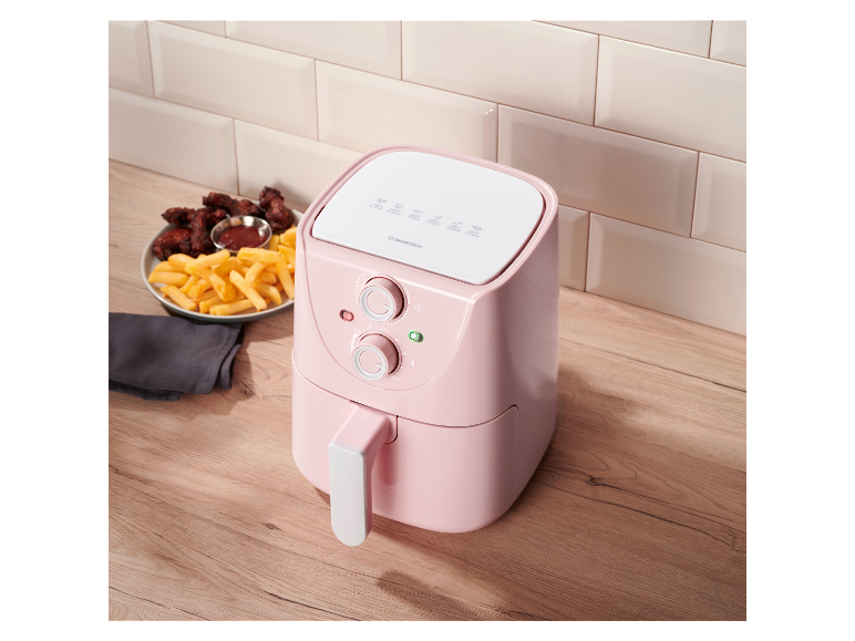Een roze Silvercrest airfryer staat op een houten tafel naast friet en kippenvleugels.