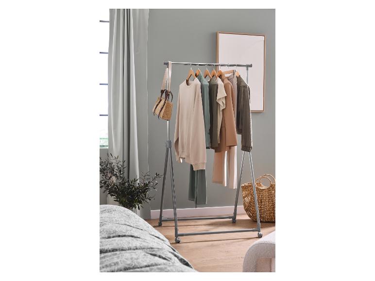 Kledingrek met kleding in diverse kleuren, een tas en een mand in een kamer.