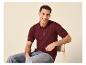 Man in een bordeauxrode gebreide poloshirt en jeans, zittend op een stoel.