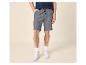 Man in blauw T-shirt en grijze shorts met trekkoord, witte sneakers.