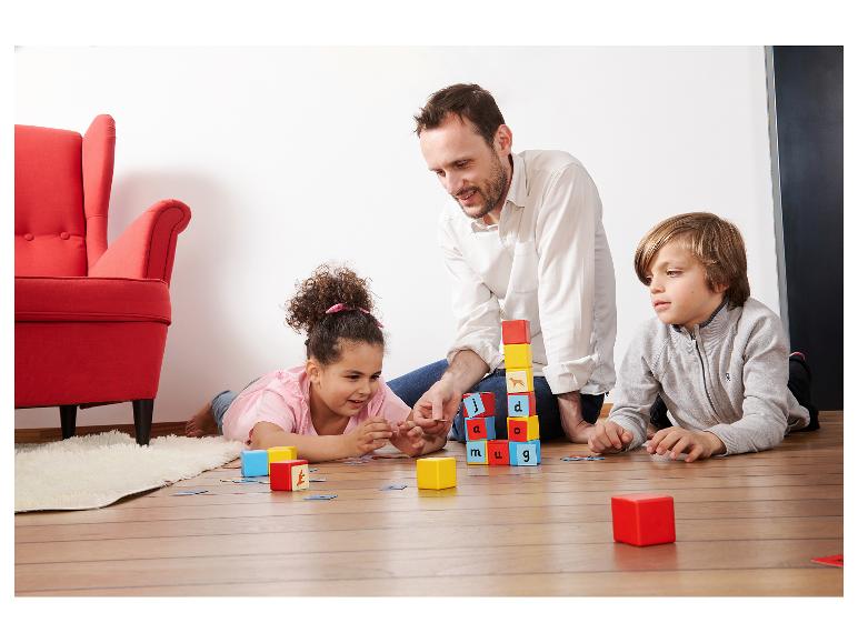 Vader en kinderen spelen op de vloer met educatieve bouwblokken en kaarten.